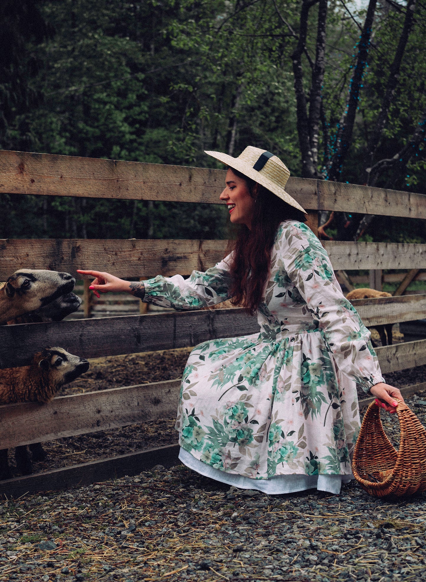Girl on a farm petting goats. She is wearing a straw hat, holding a basket and wearing a floral ivory linen dress with soft green and pink hydrangea flowers print