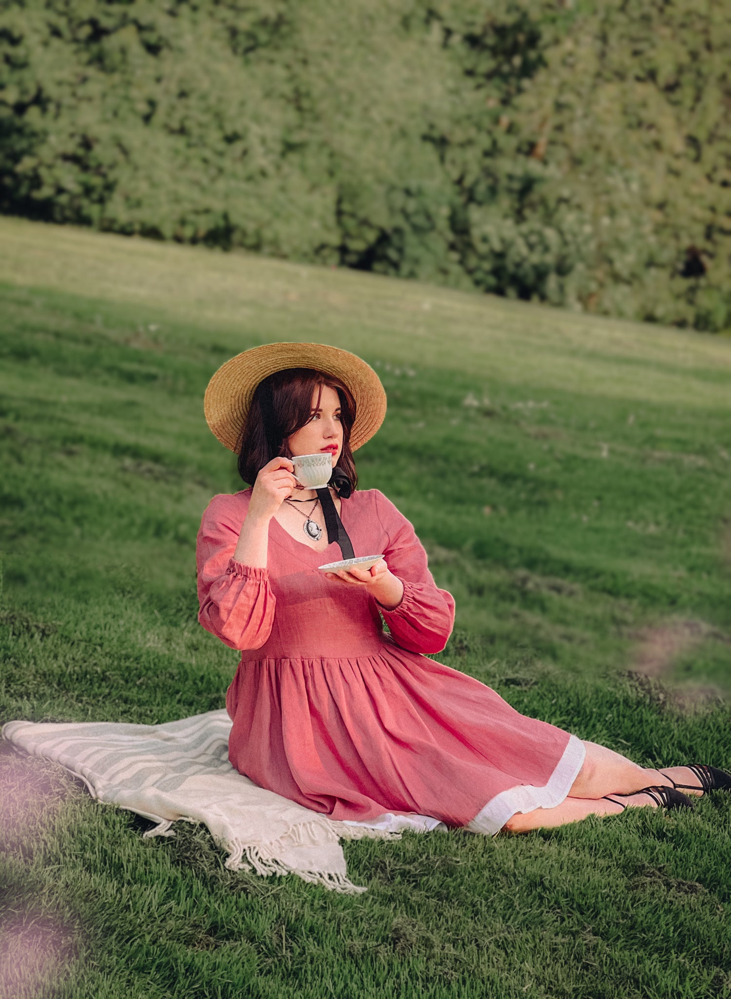 Girl having a picnic and a cup of tea on a green field wearing a Pink Linen Dress 