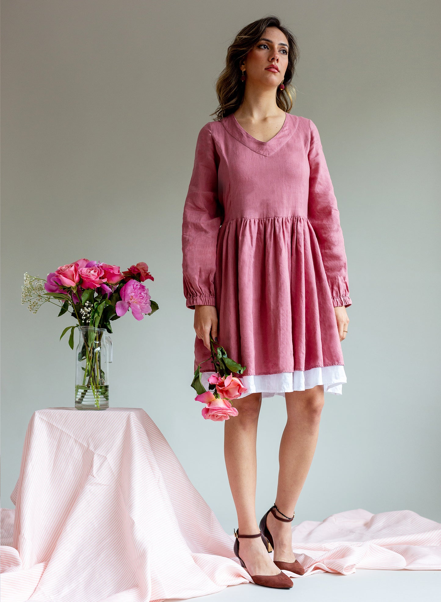 Woman wearing a V-neck short skater dress in a burnt soft pink colour with a white hem trim holding pink roses